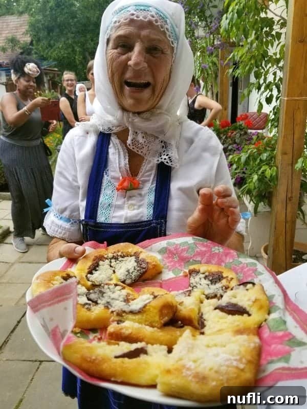 Smiling Czech grandmother holding a plate of traditional Kolaches in a rustic village setting