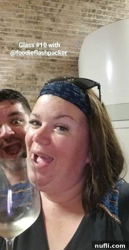 Tammilee smiling, holding a wine glass, standing next to Nathan from Foodie Flashpacker at a wine tasting event