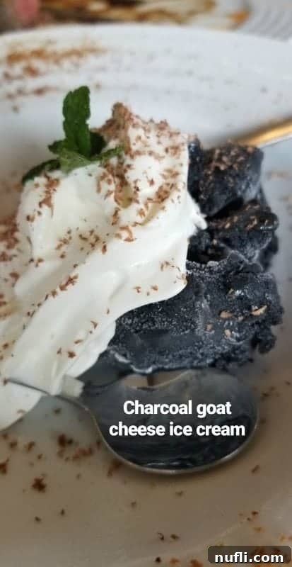 A scoop of dark charcoal goat cheese ice cream in a white bowl with a spoon