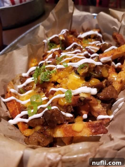 Smoky Bacon Manhattan 5 Loaded nacho fries served in a parchment-lined container, topped with green onions, cheese, and bacon, showcasing a vibrant and indulgent appetizer.