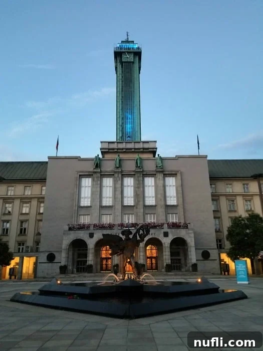 The grand New City Hall in Ostrava, featuring a prominent clock tower and a statue in the foreground, under a clear sky.