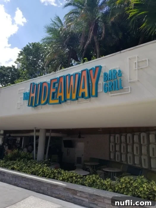The Hideaway Bar & Grill sign above an inviting outdoor seating area with string lights, near a pool