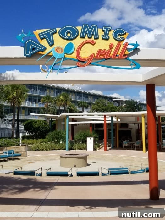 Atomic Grill sign above an outdoor dining area featuring vibrant yellow and red seating, reflecting a retro aesthetic