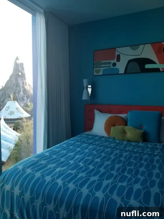 A vibrant Cabana Bay Resort room with a queen bed next to a large window offering a view of Volcano Bay waterpark