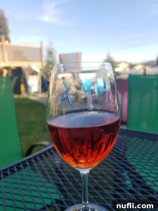 Elegant wine glass filled with red wine on a dark table next to green chairs at a Lake Chelan winery