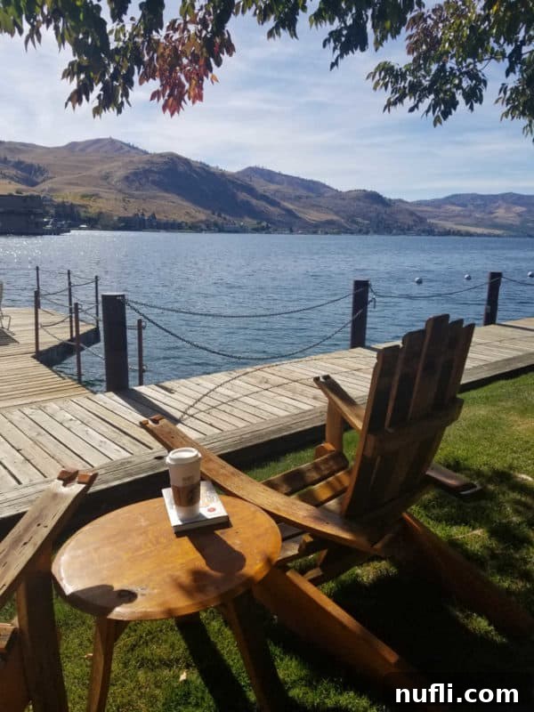 Cozy Adirondack chair and table near the tranquil Lake Chelan with a dock and mountains in the background