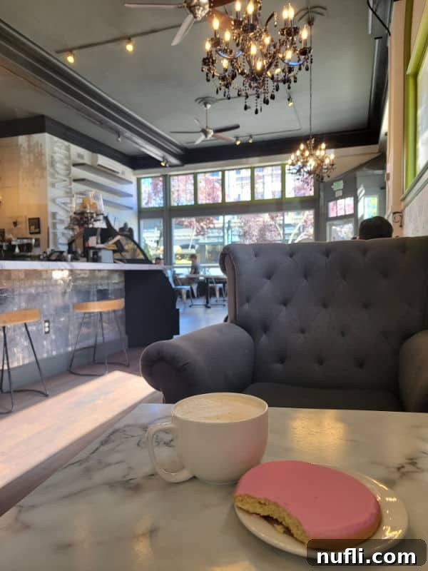 inside a coffee shop with grey chair, chai and a cookie on a white marble table, fun chandeliers overhead 
