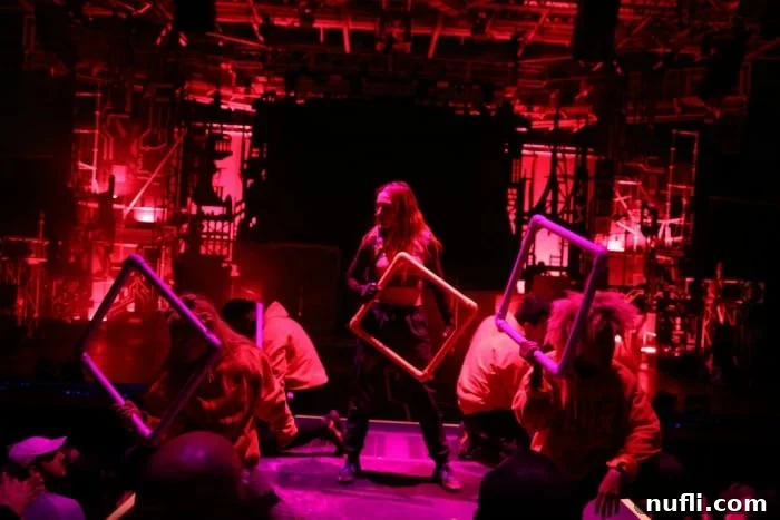 A red-lit stage featuring performers holding glowing square props, creating a futuristic visual