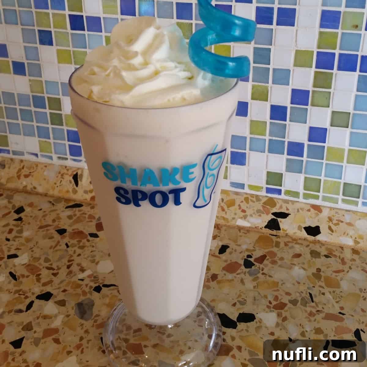 Shake spot glass with a bourbon milkshake with whipped cream garnish and a blue straw