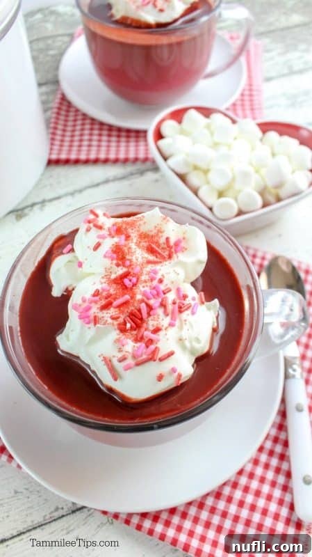 Glass coffee mug with red velvet hot chocolate next to a bowl of mini marshmallows, ready to be enjoyed.