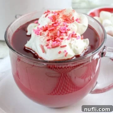 Red Velvet Hot Chocolate in a glass mug topped with whipped cream and pink sprinkles
