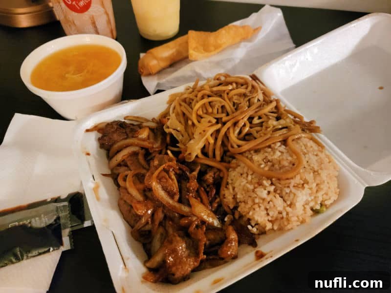 A satisfying takeout meal from Taste of China restaurant in Oakhurst, featuring Mongolian beef, noodles, and fried rice in a Styrofoam container, with a bowl of soup and an egg roll in the background.