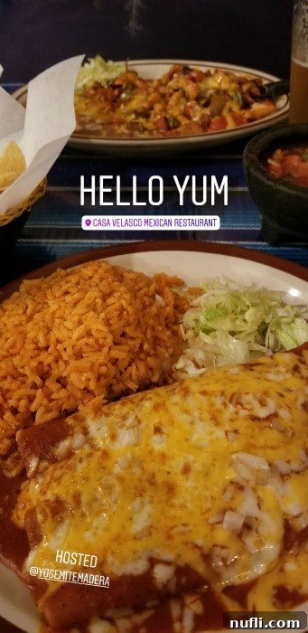Two cheese enchiladas with a side of rice on a white plate, and a second plate of food slightly blurred in the background, served at Casa Velasco Mexican Restaurant, Bass Lake.