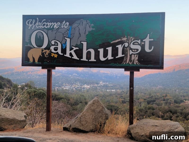 A rustic wooden sign welcoming visitors to Oakhurst, adorned with carvings of a sequoia tree, a bear, and mountains, symbolizing the area's natural beauty.