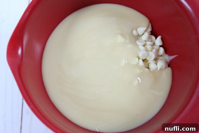 Decadent RumChata Fudge 5 A vibrant red bowl filled with creamy sweetened condensed milk and lustrous white chocolate chips, ready for mixing.