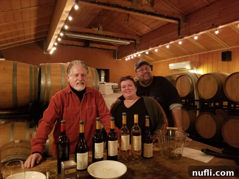 Tammilee Tips and Park Ranger John with Ray from Westbrook Wines, standing amidst wine barrels in the background.