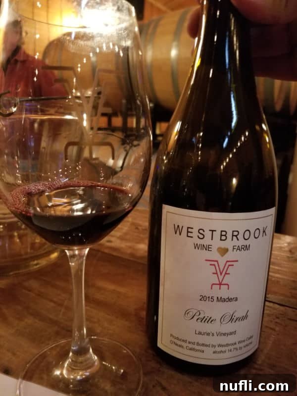 Wine glass positioned next to a 2015 Madera Westbrook Wine Farm Petite Sirah bottle, ready for tasting.
