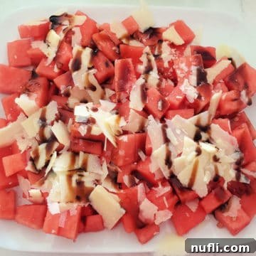 Vibrant Watermelon Salad with Pecorino cheese shavings and a drizzle of balsamic vinegar, presented in a minimalist style.