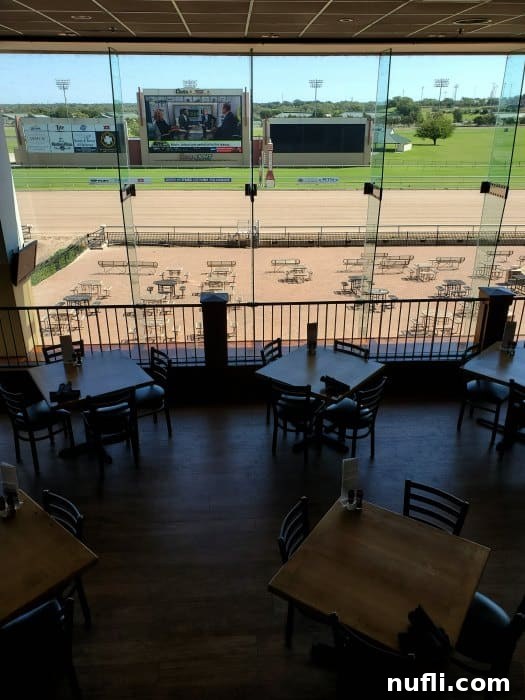 looking out at a race track with dirt track, tables and chairs and a large tv screen.