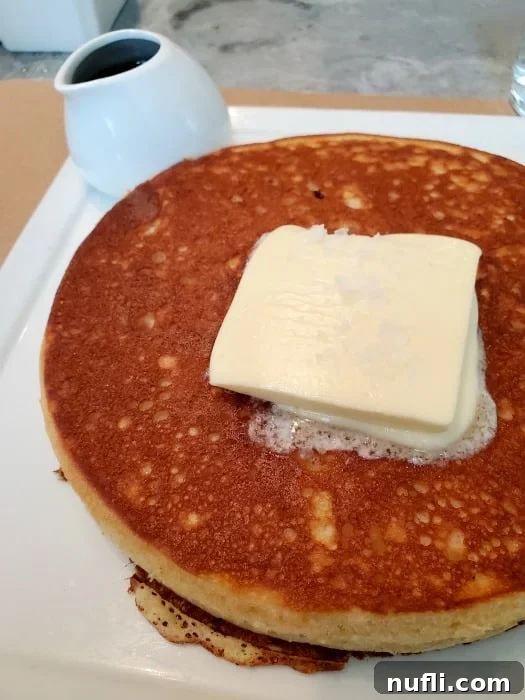 pancakes with a large square of butter on it next to a container of syrup 