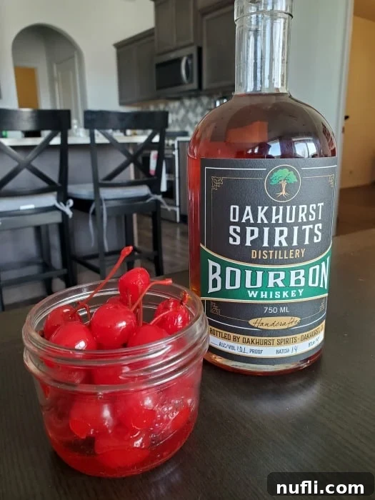 Fudgy Bourbon Cherry Brownies 4 Maraschino cherries soaking in Oakhurst Spirits Bourbon in a mason jar, with a bottle of the bourbon next to it.