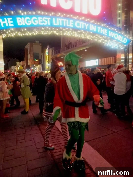 A group of people dressed as The Grinch and an elf posing joyfully under the illuminated Reno Arch during the Santa Crawl.