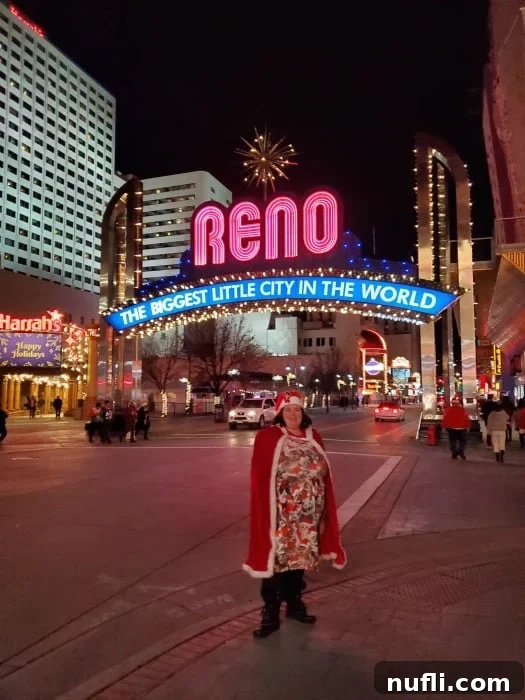 A person in a kitten Santa dress and cape standing confidently in front of the brilliantly illuminated Reno Arch, a landmark of the city.