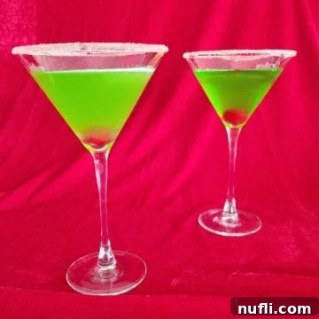 Two Bright green cocktails with cherries in them in martini glasses with a sugared rim, ready for a festive celebration.