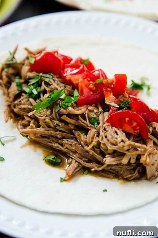 A vibrant Mexican Pulled Pork taco on a white plate, garnished with chopped tomatoes, onions, and fresh cilantro.