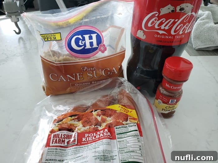 Key ingredients for Crockpot Brown Sugar Kielbasa: brown sugar, pre-sliced kielbasa sausage, a can of Coca-Cola, and a small bowl of chili powder, laid out on a white countertop.