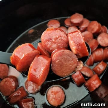 A slow cooker bowl filled with delicious brown sugar kielbasa bites, ready to be served, with a spoon for scooping.