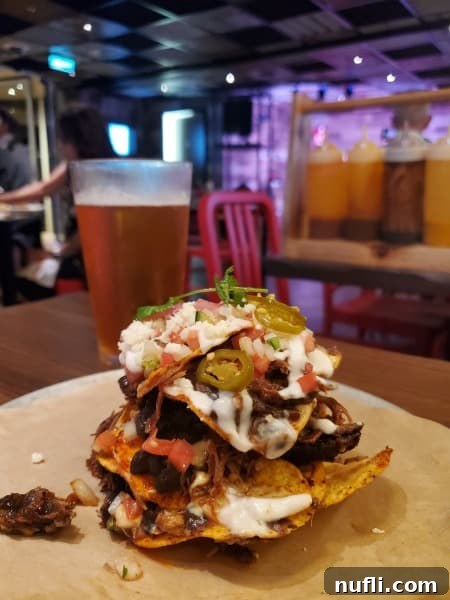 trash can nachos on a white plate next to a glass of beer