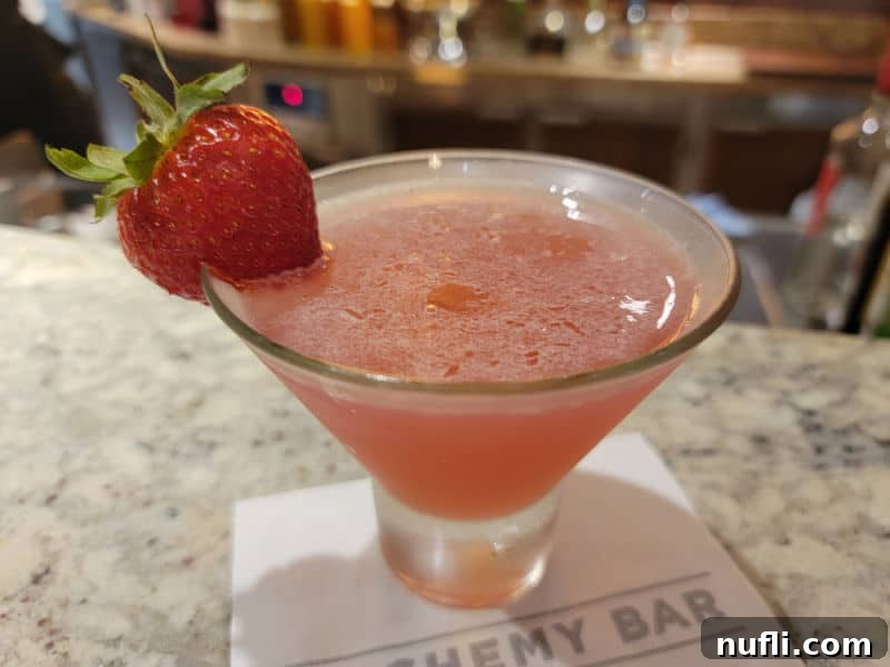 Alchemy Bar Peach Elixir 4 Curative Peach Cosmopolitan in a stemless martini glass on a white napkin with a strawberry garnish