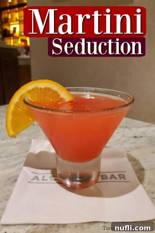 Martini Seduction text over a vibrant pink drink in a short martini glass, garnished with an orange wedge, resting on an Alchemy Bar napkin.