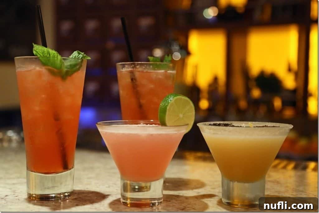 Everything You Need to Know About the Carnival Cheers Package 3 Four Alchemy Bar cocktails on a counter with lights behind them