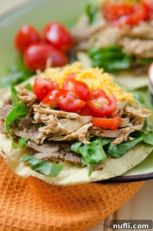 Easy Slow Cooker Mexican Chicken Tostadas 3 a plate with tostadas piled with chicken, tomatoes and cheese.