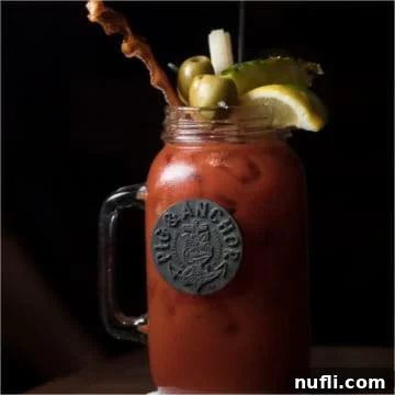 Carnival Guy's Smokin' Pig & Anchor Bloody Mary 3 bloody mary cocktail in a large mason jar glass garnished with bacon, olives, and lemon, a vibrant representation of the Pig & Anchor Bloody Mary