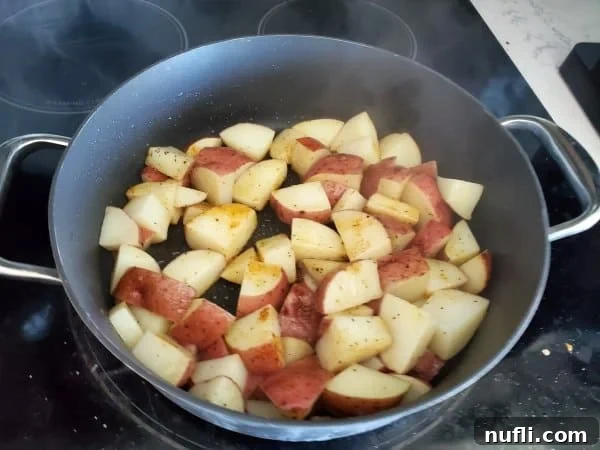 Red Breakfast Potatoes Recipe 4 Seasoned red potatoes sizzling in a dark skillet on the stovetop