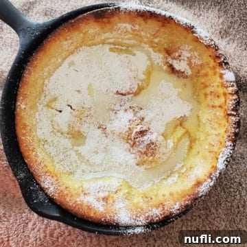 Close-up of a Lemon Dutch baby with powdered sugar in a cast iron skillet, ready to serve.