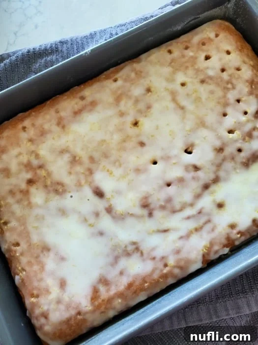 Zesty Lemon Jello Cake Recipe 3 lemon jello cake in a baking dish on top of a grey towel