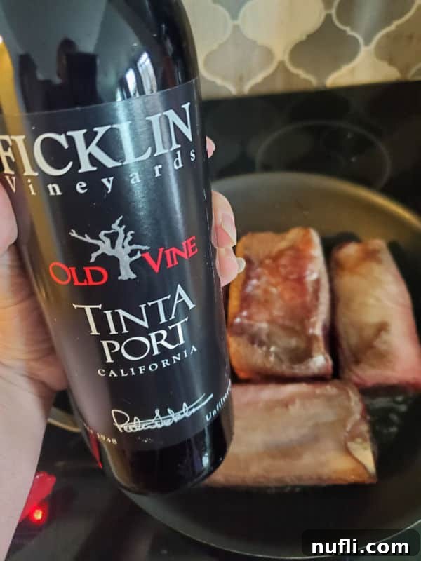 Hand holding a bottle of Ficklin Vineyards Old Vine Tinta Port over a pan with short ribs on the stovetop