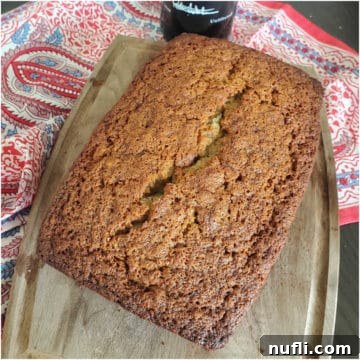A freshly baked loaf of Tinta Port Wine Banana Bread, sliced and ready to serve, rests on a wooden cutting board beside a neatly folded napkin, highlighting its inviting texture.