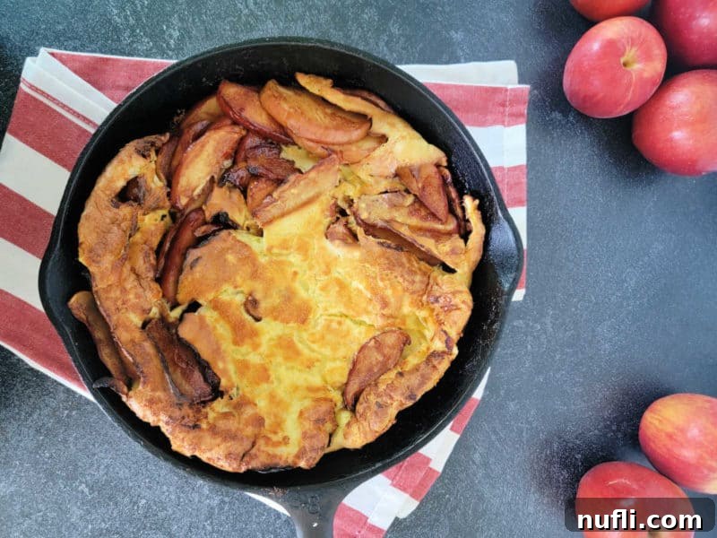 Easy German Apple Pancakes 9 German Apple Pancake in a cast iron skillet on a red striped cloth towel with apples