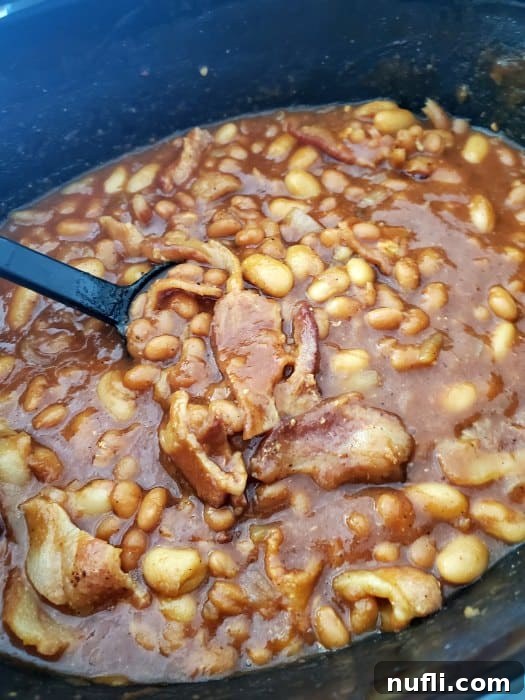 baked beans and bacon in a slow cooker bowl with a large spoon