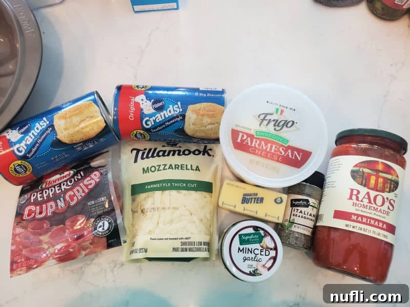 Ingredients for Pepperoni Pizza Monkey Bread laid out on a white quartz counter: grands biscuits, pepperoni, tillamook mozzarella cheese, parmesan cheese, Italian Seasoning, Minced Garlic, Rao's Homemade Marinara Sauce