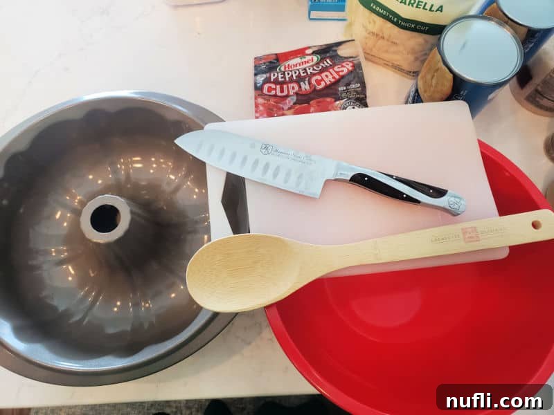 Kitchen tools needed to make Pepperoni Pizza Monkey Bread: Bundt Pan, Knife, Wooden Spoon, Red Bowl, and cutting board