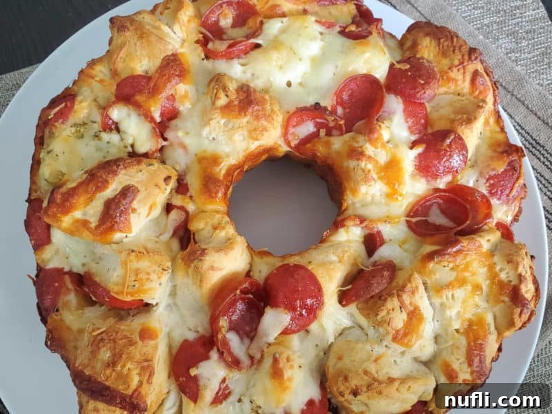 Large slice of Pepperoni Pizza Monkey Bread being pulled from the main bread, with marinara sauce in the background