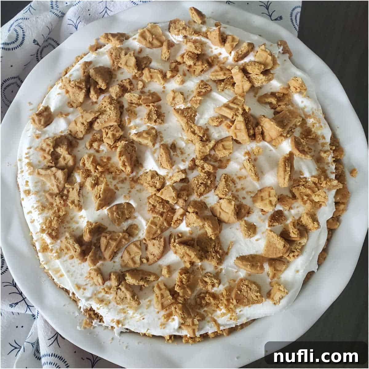 A completed Nutter Butter Banana Pudding in a white pie dish, adorned with a decorative cloth napkin, showcasing its mouth-watering layers.