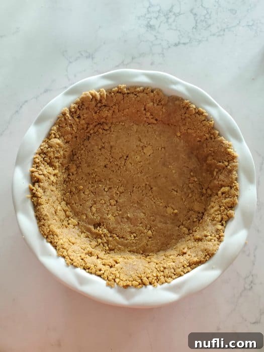 The Nutter Butter crust mixture pressed firmly into a white pie dish, forming the base of the dessert.
