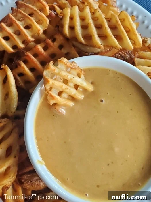 Waffle fry dipping into Chick-fil-A sauce in a white bowl on a platter with more fries